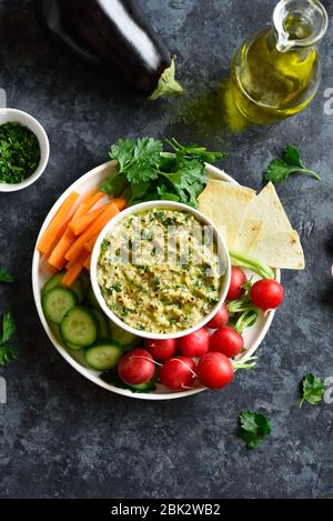 Baba ganoush (geröstete Auberginen-Dip) in Schüssel und frisches Bio-Gemüse auf dunklem Steingrund. Gesunde Ernährung. Vegetarisches veganes Food Konzept. Bis Stockfoto