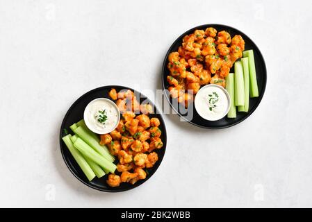 Büffelflügel aus Blumenkohl mit Sellerie und Sauce auf Platte über weißem Steinhintergrund mit freiem Textraum. Gesundes Essen, pflanzliches Lebensmittelkonzept. T Stockfoto