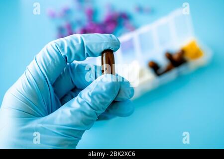 Eine Hand mit einem medizinischen Handschuh hält mehrfarbige Kapseln, eine Pillenbox mit Medikamenten auf blauem Hintergrund Stockfoto