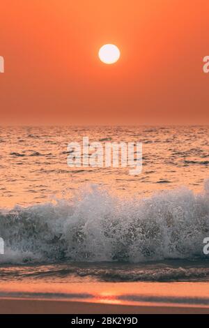 Sonnenuntergang Sonne Über Dem Meer. Natürlicher Sonnenaufgang Himmel Warme Farben Über Dem Meer. Ocean Wasser Schaum Spritzwasser Waschen Sandstrand Bei Sonnenuntergang. Stockfoto