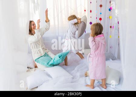 Junge Frau haben Spaß mit den Kindern spielen mit Kissen auf dem Bett im Schlafzimmer. Bleib zu Hause und Familie Konzept. Stockfoto