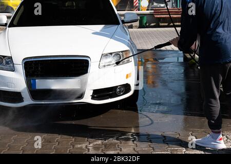 Aufnahme eines lässigen Mannes, der sein Auto unter Hochdruckwasser im Freien wäscht. Stockfoto