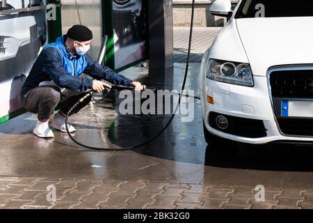 Autowäsche. Mann in Freizeitkleidung und Schutzmaske Reinigung Auto mit Hochdruckwasser und Pinsel Stockfoto