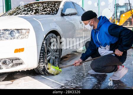 Mann in Maske Arbeiter waschen Auto-Leichtmetallräder auf einer Autowäsche Stockfoto