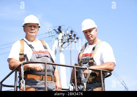 Zwei Elektroarbeiter auf einem Aufzug. Ingenieure steigen auf einen Kran, um eine Hochhausstütze zu reparieren. Männer beseitigen den Unfall an der Höhenstation Stockfoto