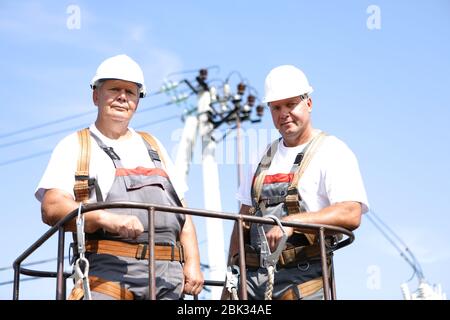 Zwei Elektroarbeiter auf einem Aufzug. Ingenieure steigen auf einen Kran, um eine Hochhausstütze zu reparieren. Männer beseitigen den Unfall an der Höhenstation Stockfoto