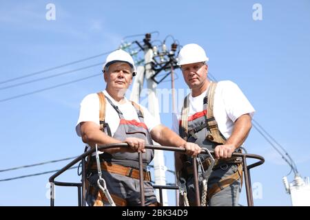 Zwei Elektroarbeiter auf einem Aufzug. Ingenieure steigen auf einen Kran, um eine Hochhausstütze zu reparieren. Männer beseitigen den Unfall an der Höhenstation Stockfoto