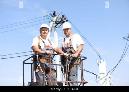 Zwei Elektroarbeiter auf einem Aufzug. Ingenieure steigen auf einen Kran, um eine Hochhausstütze zu reparieren. Männer beseitigen den Unfall an der Höhenstation Stockfoto