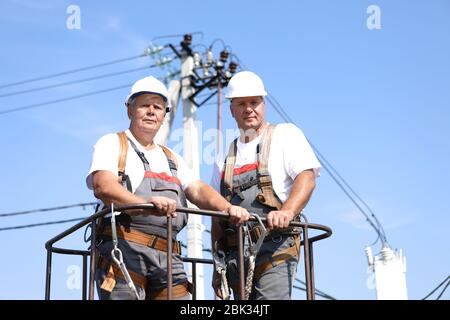 Zwei Elektroarbeiter auf einem Aufzug. Ingenieure steigen auf einen Kran, um eine Hochhausstütze zu reparieren. Männer beseitigen den Unfall an der Höhenstation Stockfoto