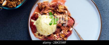 Hausgemachte Rhabarber und Erdbeere bröseln aus Haferflocken und Nüssen Topping und mit Vanille Eis Kugeln Stockfoto