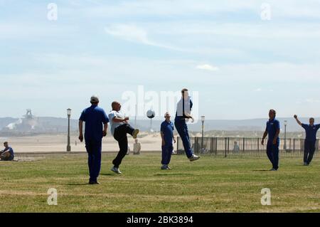 Arbeiter von Seaton Carew in der Nähe von Hartlepool spielen Fußball auf dem Rasen zur Mittagszeit, in der Ferne River Tees Mündung & Corus Stahlwerk; Teesside; NE Engla Stockfoto