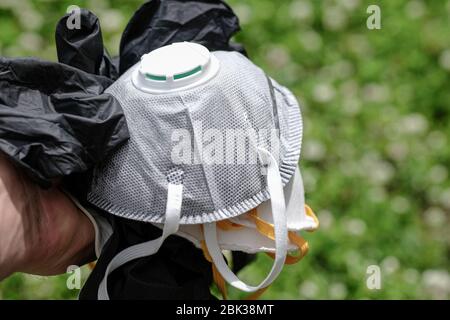 Mann halten ffp2 Schutzmaske und Handschuhe Abfall auf Grasboden.Covid Coronavirus Krankheit Müllverschmutzung Stockfoto