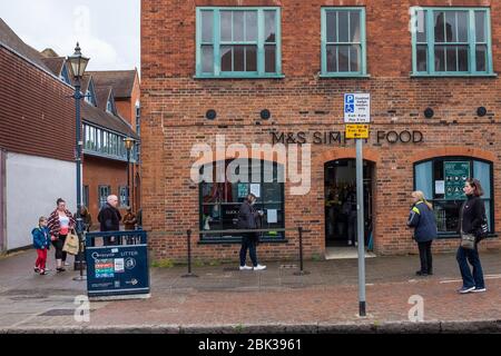 Menschen beobachten soziale Distanz während sie Schlange stehen, aber wesentliche Dinge außerhalb eines Supermarktes in Hitchin, Hertfordshire, England Stockfoto