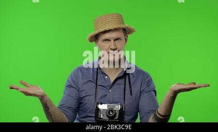 Porträt des Mannes Mode touristischen Fotografen zeigt auf etwas mit seinen Händen. Schöner Mann im Urlaub in blauem Hemd und Hut mit Retro-Kamera. Platz für Ihr Logo. Chroma-Taste. Grüner Bildschirm Stockfoto