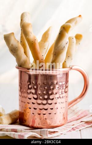 Traditionelle italienische Brotstangen mit Mohn Samen in einem Kupferbecher auf einer textilen Serviette und Holzhintergrund, Kopierraum. Frischer italienischer Snack. Stockfoto