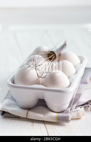 Frisch gepflückte Bio-Bauernhof Hühnereier in einem Keramiktablett auf einem Holzhintergrund mit Metall Schneebesen und Textil-Handtuch, kopieren Raum. Gesunde natürliche Lebensmittel Stockfoto