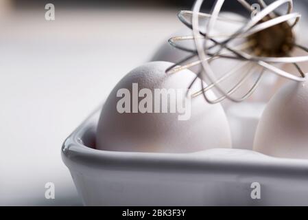 Frisch gepflückte Bio-Bauernhof Hühnereier in einem Keramiktablett auf einem Holzhintergrund mit Metall Schneebesen und Textil-Handtuch, kopieren Raum. Gesunde natürliche Lebensmittel Stockfoto