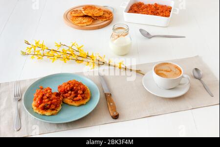 Tisch mit hausgemachten würzigen gebackenen Bohnen mit Speck und Kartoffelbröseln, Tasse Kaffee, Glas Sahne, mit wenigen Zweigen von goldenem Regen verziert. Englisch Stockfoto