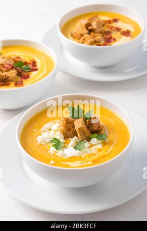 Butternuss-Kürbiscremesuppe mit Milchcreme, Speck, Croutons, Feta-Käse und Petersilie. Vorderansicht Stockfoto