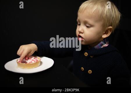 Ein kleiner blonder Junge isst Süßigkeiten. Köstliches Tartlet. Stockfoto