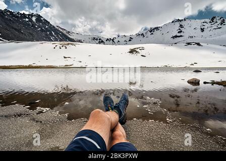 Die Beine des Menschen in Tracking Schuhe und Blick auf die schneebedeckten Gletscher auf dem See in die Berge Stockfoto