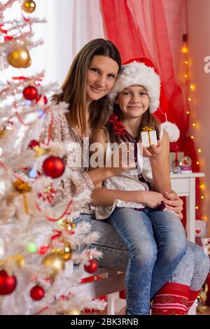 Glückliche Mutter und Tochter sitzen in einem wunderschön eingerichteten Zimmer in der Nähe eines Weihnachtsbaums Stockfoto