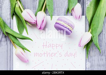 Grußkarte zum Muttertag. Rosa Tulpen und violettes Makaron auf grauem Holzhintergrund Stockfoto