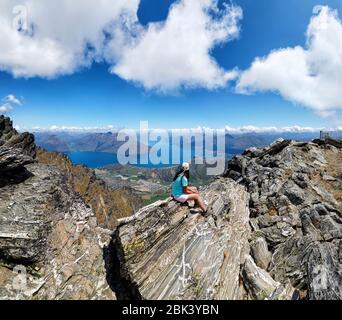 Wanderer sitzt auf Felsen der Remarkables Bergkette, Queenstown, Otago, South Island, Neuseeland, Ozeanien. Stockfoto