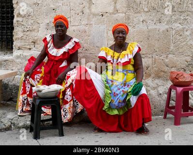 Cartagena, Kolumbien, 1. August 2019: Zwei typische Obsthändler palenqueras mit bunten Kleidern sitzen von der Vorderseite ruhen Stockfoto