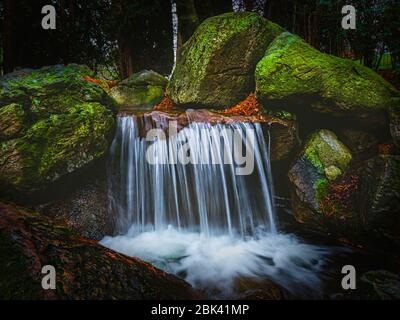 Schöner Wasserfall mit verschwommenem Wasser, umgeben von moosigen Felsbrocken. Landschaftsgestaltung des japanischen Gartens. Wunderschöne Landschaft mit kleinem Teich und Wasserfall. Stockfoto