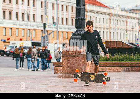 Moskau, Russland - 7. JULI 2017: Junger Skateboarder in Shorts, der einen Springen gegen eine Menschenmenge macht, die eine Straße überquert Stockfoto