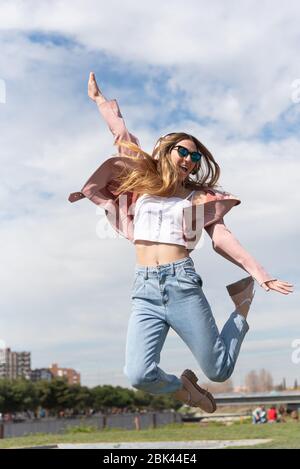 Das junge kaukasische Mädchen hört gern Musik, die vor Freude in einem Park in der Stadt springt. Stockfoto