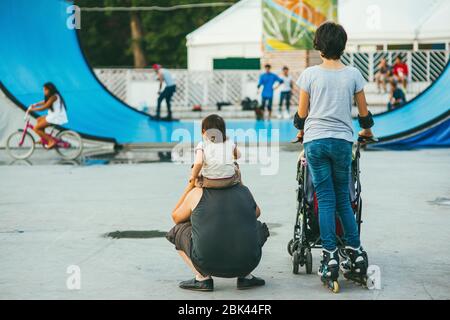 Moskau, Russland - 9. AUGUST 2014: Junge Sportlerin Mama reitet auf einem Skateboard im Sokolniki Park, während ihr Mann ein Kind am Hals hält Stockfoto