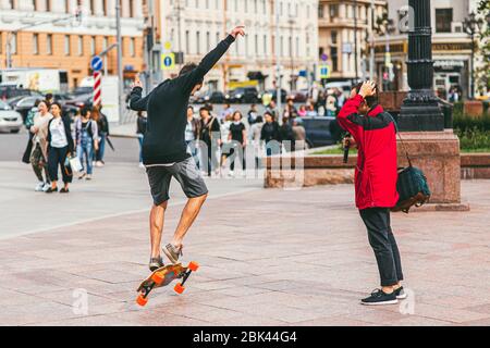 Moskau, Russland - 7. JULI 2017: Junger Skateboarder in Shorts, der einen Springen gegen eine Menschenmenge macht, die eine Straße überquert Stockfoto