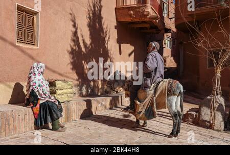 Ein alter Mann sitzt auf einem Esel und spricht mit einer Frau in traditioneller Kleidung im Dorf Abyaneh, Provinz Esfahan, Iran, Persien, Naher Osten Stockfoto