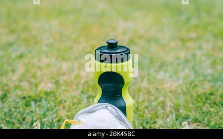 Wasserflasche für Sport mit einer Maske, um nach draußen zu gehen. Sport im Park durch Schutzmaßnahmen gegen das Coronavirus zu machen. Stockfoto