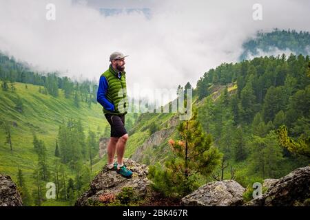 Ein Mann steht auf einem Hügel vor einem nebeligen Bergtal. Neblige Wetter hoch in den Bergen im Sommer Stockfoto