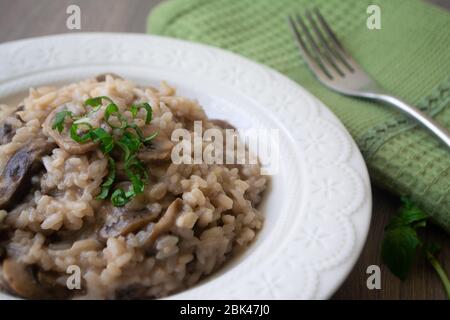 Klassisches italienisches veganes Pilzrisotto mit arborio Reis, Pilzen, Zwiebeln und Knoblauch, garniert mit Basilikumbändchen auf einer rustikalen Holzoberfläche mit viel Geschmack Stockfoto