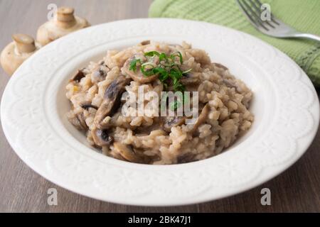 Klassisches italienisches veganes Pilzrisotto mit arborio Reis, Pilzen, Zwiebeln und Knoblauch, garniert mit Basilikumbändchen auf einer rustikalen Holzoberfläche mit viel Geschmack Stockfoto