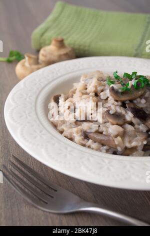 Klassisches italienisches veganes Pilzrisotto mit arborio Reis, Pilzen, Zwiebeln und Knoblauch, garniert mit Basilikumbändchen auf einer rustikalen Holzoberfläche mit viel Geschmack Stockfoto