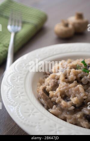 Klassisches italienisches veganes Pilzrisotto mit arborio Reis, Pilzen, Zwiebeln und Knoblauch, garniert mit Basilikumbändchen auf einer rustikalen Holzoberfläche mit viel Geschmack Stockfoto