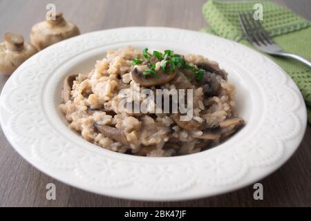 Klassisches italienisches veganes Pilzrisotto mit arborio Reis, Pilzen, Zwiebeln und Knoblauch, garniert mit Basilikumbändchen auf einer rustikalen Holzoberfläche mit viel Geschmack Stockfoto