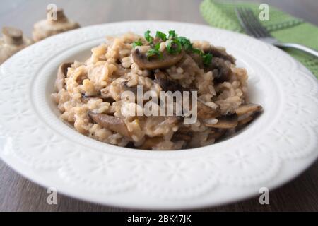 Klassisches italienisches veganes Pilzrisotto mit arborio Reis, Pilzen, Zwiebeln und Knoblauch, garniert mit Basilikumbändchen auf einer rustikalen Holzoberfläche mit viel Geschmack Stockfoto
