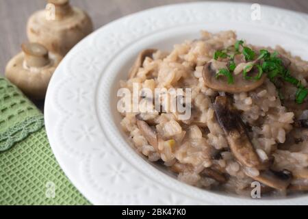 Klassisches italienisches veganes Pilzrisotto mit arborio Reis, Pilzen, Zwiebeln und Knoblauch, garniert mit Basilikumbändchen auf einer rustikalen Holzoberfläche mit viel Geschmack Stockfoto