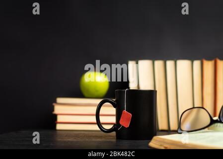 Stapel von Büchern mit einer Tasse Tee zum Lesen auf einem dunklen Tisch mit Kopierraum Stockfoto