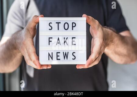Fake News Infosemics during Covid-19 Pandemie Concept. Mann Hände halten Leuchtkasten mit Text Stoppen Fake News im Vordergrund. Die Leute wollen den Trut kennen Stockfoto