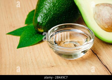 Schüssel mit Öl und reife frische Avocado auf Holztisch Stockfoto