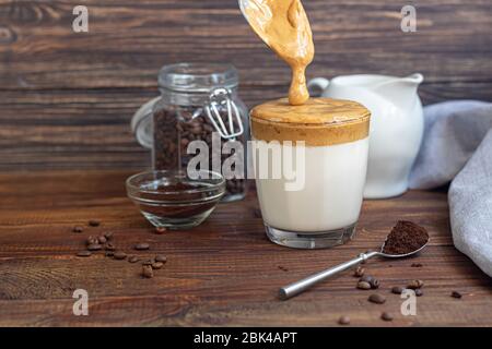 Dalgona Kaffee ist ein trendiges kaltes koreanisches Getränk. Geschmackvoller, aromatischer Kaffee mit Milch und Zucker in einem Glas auf Holzuntergrund. Kopierbereich Stockfoto