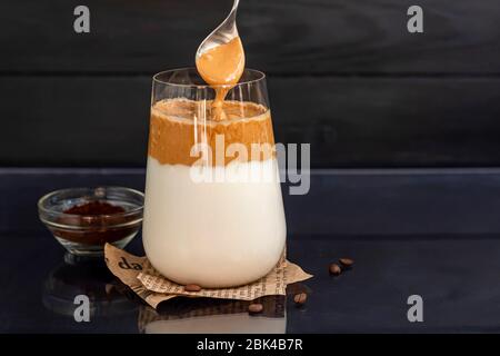 Dalgona Kaffee ist ein trendiges kaltes koreanisches Getränk. Geschmackvoller, aromatischer Kaffee mit Milch und Zucker in einem Glas auf schwarzem Hintergrund. Kopierbereich Stockfoto