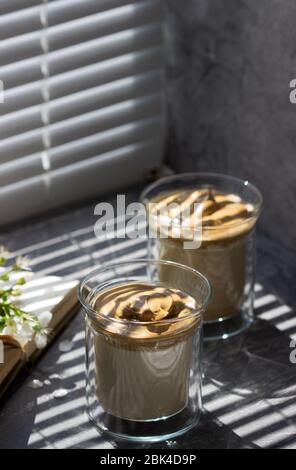 Dalgona Kaffee in transparenten Gläsern auf einer Fensterbank, die von Sonnenlicht beleuchtet wird. Stockfoto